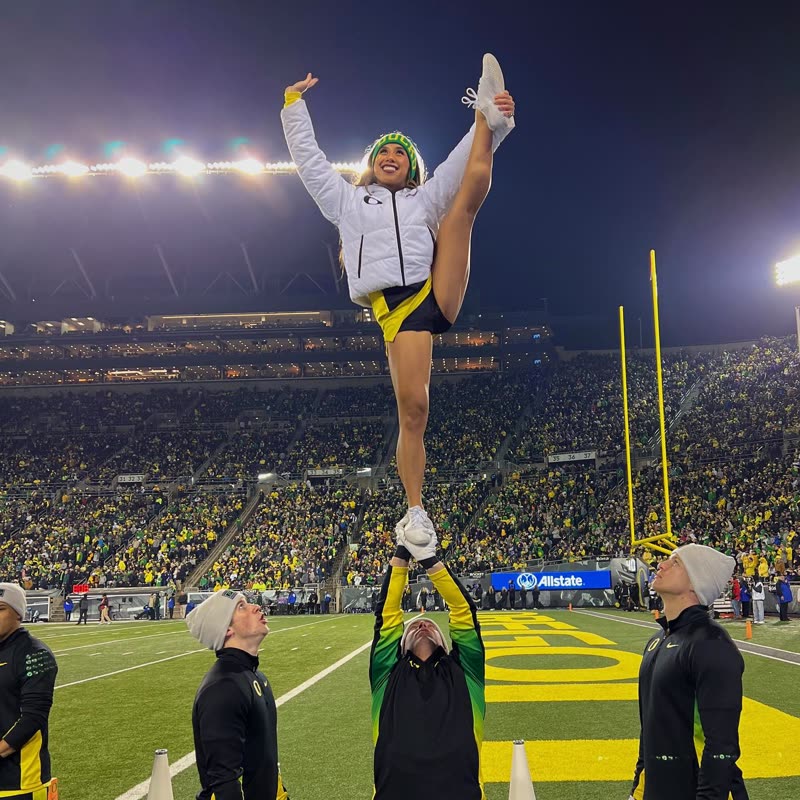 Melodi at the top of a stunt under the Autzen lights